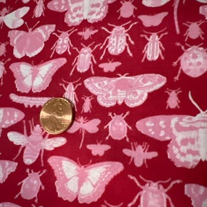 Peut inclure: Tissu rouge avec un motif de papillons et d'insectes roses et blancs. Le tissu est texturé et a un léger brillant.