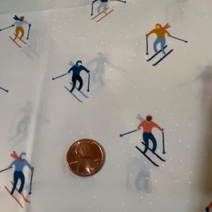 May include: White fabric with a repeating pattern of skiers in various colors. The skiers are wearing blue, red, and yellow clothing. The fabric has a subtle white dot pattern.