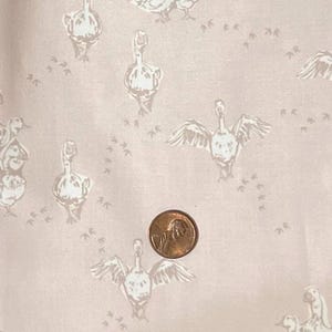 May include: Pale pink fabric featuring a repeating pattern of white geese and footprints. A copper penny is placed on the fabric for scale. The geese are shown in different poses, some with wings outstretched.