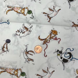 May include: White fabric featuring a repeating pattern of cartoon cats in different poses. The cats are brown, tan, and black, some playing with balls of yarn. The yarn is green, blue, and red. A penny is in the center.