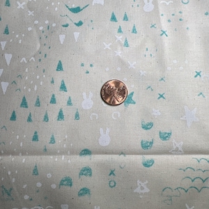 May include: A close-up of a beige fabric with a repeating pattern of teal and white shapes. The shapes include triangles, circles, wavy lines, and bunny rabbits. A copper penny is placed on the fabric.