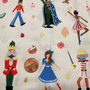 May include: A white fabric with a repeating pattern of whimsical Nutcracker-themed illustrations. The design includes a toy soldier, a magician, a ballerina, a nutcracker, and a mouse king, along with sweets and stars.