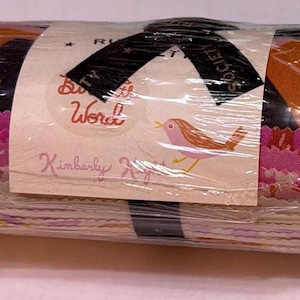 May include: A fabric jelly roll bundle wrapped in clear plastic with a black ribbon. The paper label features a small bird illustration, the text "Ruby Star Society", "Birdie the Word", and "Kimberly Kight". The fabric layers show pink, orange, and white patterns.