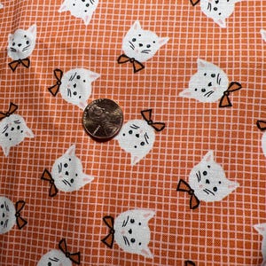 Puede incluir: Tela naranja con un patrón repetido de gatos blancos con lazos negros. Los gatos miran hacia adelante con los ojos cerrados.