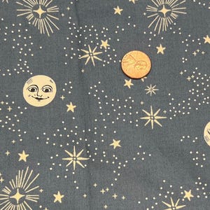 May include: Blue fabric with a celestial design featuring smiling moons, stars, and constellations in cream. The fabric has a whimsical, night sky theme, with a penny for scale.