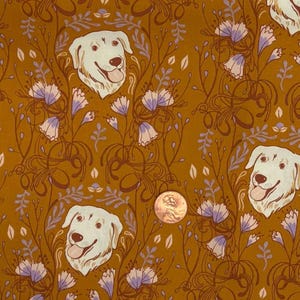 May include: A mustard yellow fabric featuring a repeating pattern of white dog heads with tongues out, surrounded by light purple bell-shaped flowers and dark brown swirling stems. A copper penny is placed on the fabric for scale.