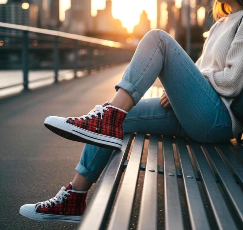 Pu&ograve; includere: Sneakers alte con tomaia in tessuto a quadri rosso e nero, lacci bianchi e punta e suola in gomma bianca. Le scarpe sono indossate con jeans azzurri e un maglione in maglia color crema, che mostrano uno stile di calzature casual classico.