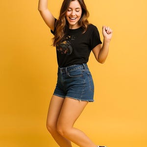 Pu&ograve; includere: Una t-shirt nera a maniche corte con una stampa grafica sul petto, abbinata a pantaloncini di jeans blu con orlo sfrangiato e sneakers alte a quadri rossi e neri con lacci bianchi e suole in gomma bianca.