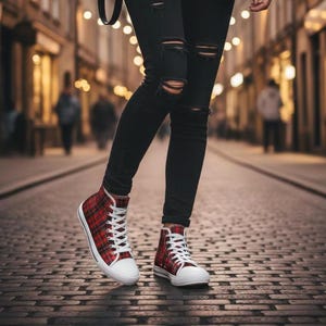 Pu&ograve; includere: Sneakers alte con motivo tartan rosso e nero, lacci bianchi e punte in gomma bianca, indossate con jeans skinny neri strappati con tagli orizzontali sulle ginocchia, su uno sfondo urbano sfocato.