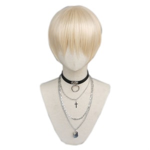 May include: A mannequin head with a short, light blonde wig and a black choker necklace with a silver ring. Below the choker are layered silver necklaces, including a cross pendant and a crystal-like charm.