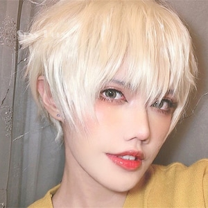 May include: A close-up portrait of a person with short, layered, light blonde hair. The person has light skin, green eyes, and is wearing a yellow sweater. The lips are painted with red lipstick.
