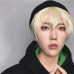 May include: A person wearing a black beanie and a black hooded sweatshirt with a green lining. The person has short, light blonde hair and is looking directly at the camera.
