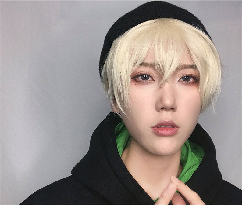 May include: A person wearing a black beanie and a black hooded sweatshirt with a green lining. The person has short, light blonde hair and is looking directly at the camera.