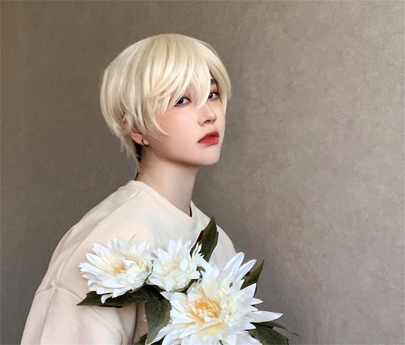 May include: A person wearing a short, layered, blonde wig. The person is holding a bouquet of white flowers with green leaves. The person is wearing a light-colored shirt. The background is a solid, neutral color.