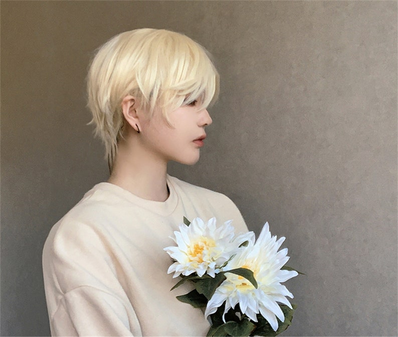 May include: A person wearing a light beige sweatshirt and a short, layered, light blonde wig. The person is holding two white and yellow artificial flowers with green leaves.