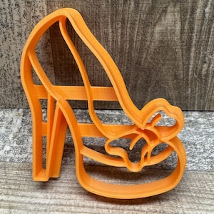 Könnte beinhalten: Ein orangefarbener Ausstecher aus Kunststoff in Form eines High-Heel-Schuhs. Der Ausstecher hat ein detailliertes Design, einschließlich Absatz, Sohle und Riemen. Der Ausstecher besteht aus strapazierfähigem Kunststoff und ist zum Backen bestimmt. Misst ca. 15 cm lang.