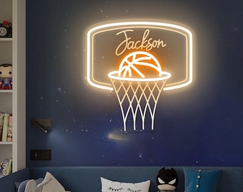 May include: A neon basketball hoop sign with the name "Jackson" in cursive script. The sign is a warm, glowing orange color and is mounted on a dark blue wall. The basketball net is white.