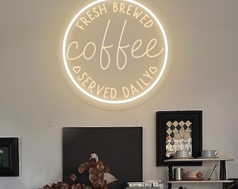 May include: A white neon sign with the text "Fresh Brewed Coffee Served Daily" in a circular shape. The sign is hanging on a white wall above a wooden cabinet with a coffee maker and other items.