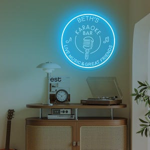 May include: A blue neon sign for "Beth's Karaoke Bar" with a microphone graphic and the text "Live Music & Great Friends." The sign is circular and mounted on a wall. A wooden cabinet with a record player, clock, and guitar are in the foreground.
