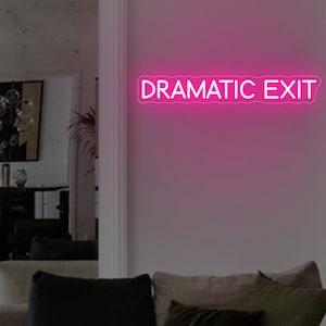 May include: A pink neon sign that reads "DRAMATIC EXIT" is mounted on a wall. The sign is in a rectangular shape and is the focal point of the image. Below the sign is a sofa with black and green pillows.