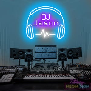 Puede incluir: Un letrero de neón con el texto "DJ Jason" en morado, enmarcado por un contorno azul de auriculares. Debajo del texto hay una forma de onda blanca. El letrero está sobre una configuración de DJ con altavoces y una mesa de mezclas.