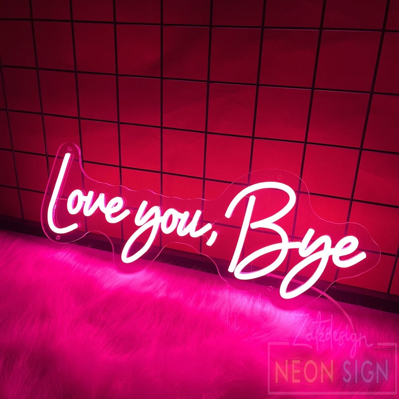 May include: A neon sign with the words "Love you, Bye" in a cursive font. The sign is white and mounted on a clear acrylic backing. The background is a red tiled wall and pink fluffy surface.