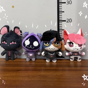 May include: Four plush toys standing in a row against a wall with a vertical measurement scale marked up to 30 cm. The figures include a black mouse-like character, a purple hooded creature, a calico cat in a black hat, and a white fox-like figure.