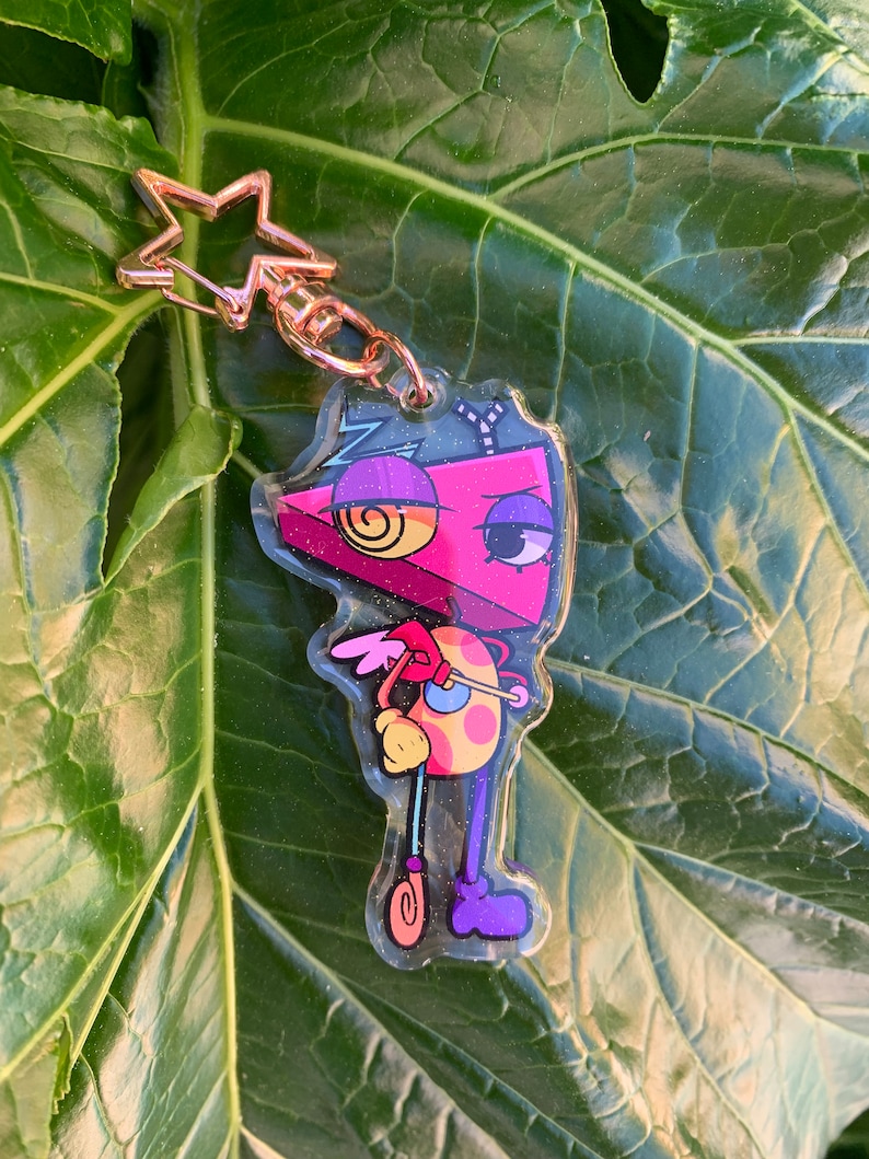 May include: A pink, yellow, and purple cartoon character keychain with a star-shaped charm. The character has a single large eye and a swirl design on its head.