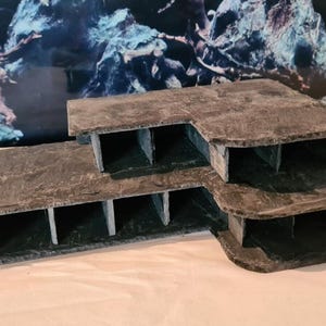 Könnte beinhalten: Mehrstufige, dunkelgraue Aquariendekoration mit strukturiertem, steinähnlichem Aussehen. Die Struktur verfügt über mehrere Ebenen und Fächer, die Schutz und visuelles Interesse in einer aquatischen Umgebung bieten sollen.