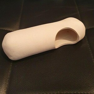 Könnte beinhalten: Ein hellbeige zylindrisches Objekt mit abgerundetem Ende und einem gebogenen Ausschnitt. Das Objekt liegt auf einer schwarzen, strukturierten Oberfläche. Die Form deutet auf ein Massagegerät oder ein ergonomisches Gerät hin.