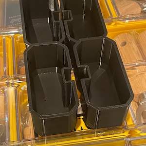 May include: Four black plastic storage containers with a grid pattern, designed to fit into a larger storage system.