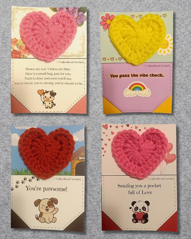 May include: Four greeting cards with crocheted heart accents. Each card features a different colored heart: pink, yellow, red, and another pink. The cards have various messages and illustrations, including a cow, a dog, a panda, and a rainbow.