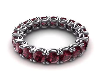 May include: A silver eternity ring featuring a continuous row of round, deep red gemstones. The gemstones are set in a polished silver band, creating a classic and elegant design. The ring is displayed against a white background.