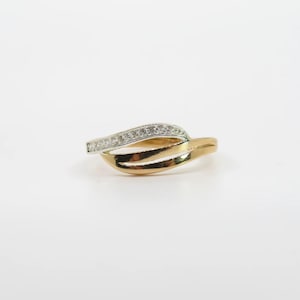 Puede incluir: Un anillo de oro y plata con un diseño único y fluido. El anillo presenta una banda de pequeñas piedras transparentes engastadas en plata, que se curva sobre una banda de oro. La banda de oro tiene un diseño de doble bucle.