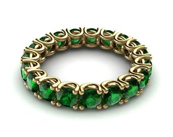 May include: A gold band ring featuring a continuous row of vibrant green emeralds. The ring's design showcases a classic eternity style, with each emerald securely set in a gold bezel. The gemstones are evenly spaced, creating a seamless, elegant look.