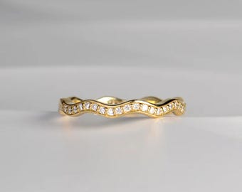 May include: A gold-colored ring with a wavy design, set with small, clear gemstones. The ring's band has a continuous, undulating pattern, creating a flowing aesthetic. The gemstones are evenly spaced along the ring's surface, reflecting light.