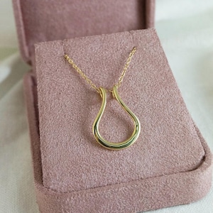 May include: A gold-colored pendant necklace with a teardrop-shaped design. The necklace is displayed in a pink velvet jewelry box. The pendant hangs from a delicate gold chain, creating a simple yet elegant look.