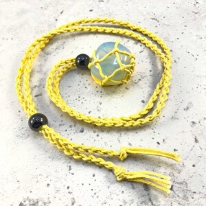 May include: A yellow macrame cord necklace with a light blue and white gemstone in a macrame net. The necklace has two black beads.