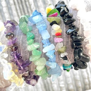 Puede incluir: Una colecci&oacute;n de ocho pulseras de chips de piedras preciosas, cada una con un color y tipo de piedra diferente. Las pulseras est&aacute;n apiladas en la mu&ntilde;eca de una persona, mostrando la variedad de colores y texturas. Las pulseras incluyen amatista, aguamarina, aventurina verde, obsidiana negra, cuarzo transparente, cuarzo rosa y jaspe amarillo.
