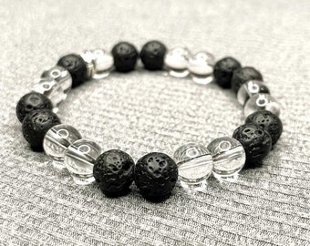 Puede incluir: Un brazalete de cuentas de roca volcánica negra y cuarzo transparente. El brazalete está hecho con cuentas negras y transparentes alternadas.