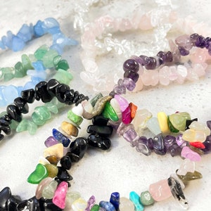 Puede incluir: Una colecci&oacute;n de pulseras de piedras preciosas de colores, incluyendo piedras negras, verdes, rosas, moradas y azules. Las pulseras est&aacute;n hechas de peque&ntilde;as piedras de forma irregular.