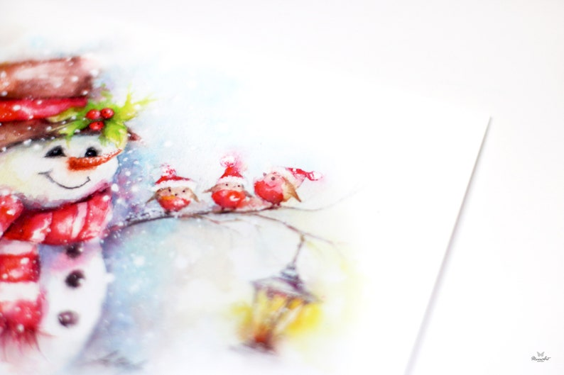 May include: Watercolour painting of a snowman wearing a red scarf and hat, standing in the snow with three red robins wearing Santa hats perched on a branch.