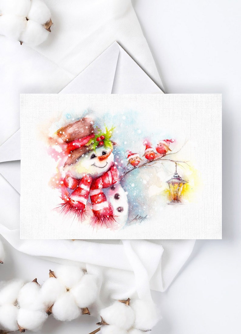 May include: A watercolour painting of a snowman wearing a red and white striped scarf and a brown hat with holly. Three red robins are perched on a branch with a lantern hanging nearby.