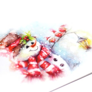 May include: A watercolour painting of a snowman wearing a red and white striped scarf and a brown hat with holly berries. The snowman is smiling and has a black button nose. The background is a snowy winter scene with a blue sky and a few snowflakes.