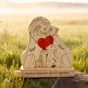 Könnte beinhalten: Holzskulptur einer Löwenfamilie mit zwei Jungen und einem roten Herz. Die Namen "Papa", "Mama", "Julie" und "Finley" sind eingraviert. Auf dem Sockel steht "Home is wherever we are together".