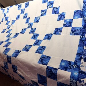 K&ouml;nnte beinhalten: Eine handgefertigte Steppdecke mit einem wei&szlig;en und blauen Blumenmuster. Die Steppdecke hat ein Schachbrettmuster mit wei&szlig;en Quadraten und blauen Blumenquadraten. Der Rand ist ein blaues Blumenmuster. Die Steppdecke ist aus weichem Stoff.