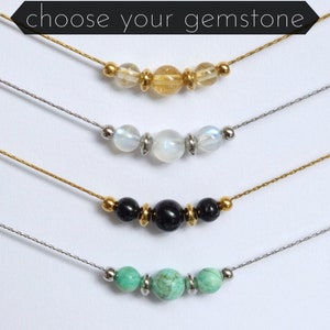 Puede incluir: Cuatro collares con diferentes cuentas de piedras preciosas. Los collares están sobre un fondo blanco. El texto "elige tu piedra preciosa" está en la parte superior de la imagen.