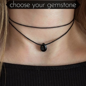 May include: A black choker necklace featuring a teardrop gemstone pendant. The necklace has two strands and is worn around the neck. The image includes the text "choose your gemstone" at the top.