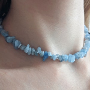 May include: A light blue aquamarine chip necklace. The necklace is made of small, irregularly shaped, light blue aquamarine stones strung together. The stones vary in size and shade, creating a natural look. The necklace is worn around the neck.