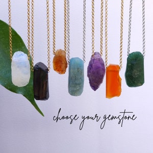 Könnte beinhalten: Sieben Halsketten mit verschiedenen Edelsteinanhängern, darunter Amethyst, Aquamarin, schwarzer Turmalin, Citrin, Mondstein, Karneol und grüner Aventurin. Die Halsketten befinden sich auf einem weißen Hintergrund mit dem Text "Wählen Sie Ihren Edelstein".